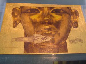 Golden face artwork with surreal fish element.
