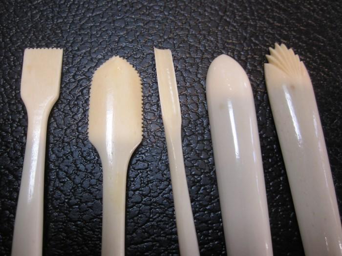 Five pottery tools on textured surface.