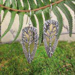Tree-themed earrings hanging from a fern.