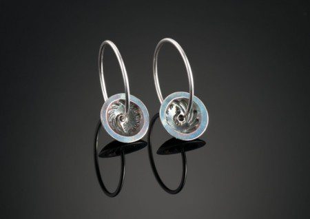 Silver hoop earrings on dark reflective surface.
