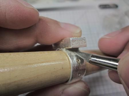 Engraving a silver ring on wooden mandrel.