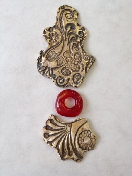 Ornate metal pieces with red circular bead.