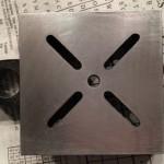 Metal square with cross-shaped cutouts on paper.