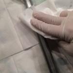 Gloved hand cleaning metal rod with cloth.