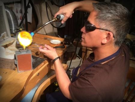 Person crafting glass with blowtorch and tools.