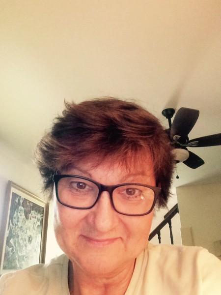 Person wearing glasses, smiling indoors near stairway.