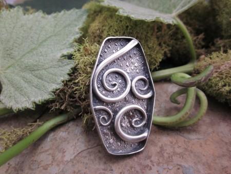Silver pendant with swirling design and leaves.