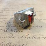 Silver ring with red gemstone on paper.