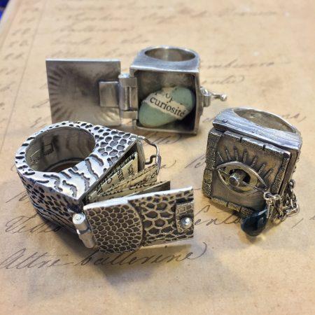 Silver rings with intricate designs and compartments.